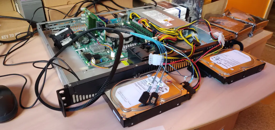 Otwarty serwer z widoczną płytą gł&oacute;wną, chłodzeniem CPU, modułami RAM oraz dwoma dyskami podłączonymi kablami SATA poza obudową